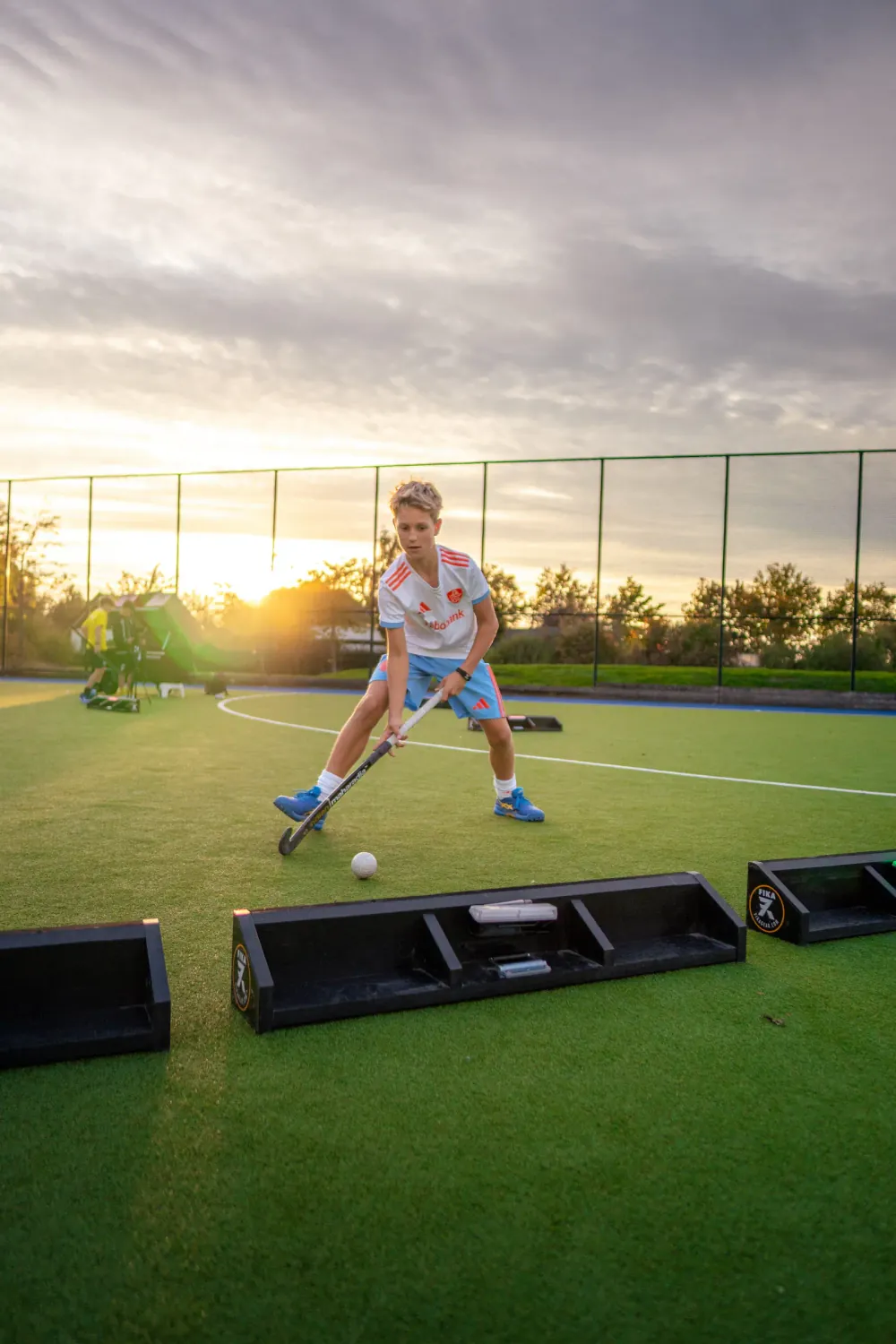 Jonge hockeyer dribbelt bij zonsondergang langs een rij X-Skills rebounders